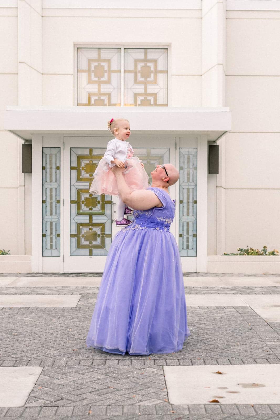 Cancer survivor picture in a purple gown, holding up her little girl in a little pink dress.